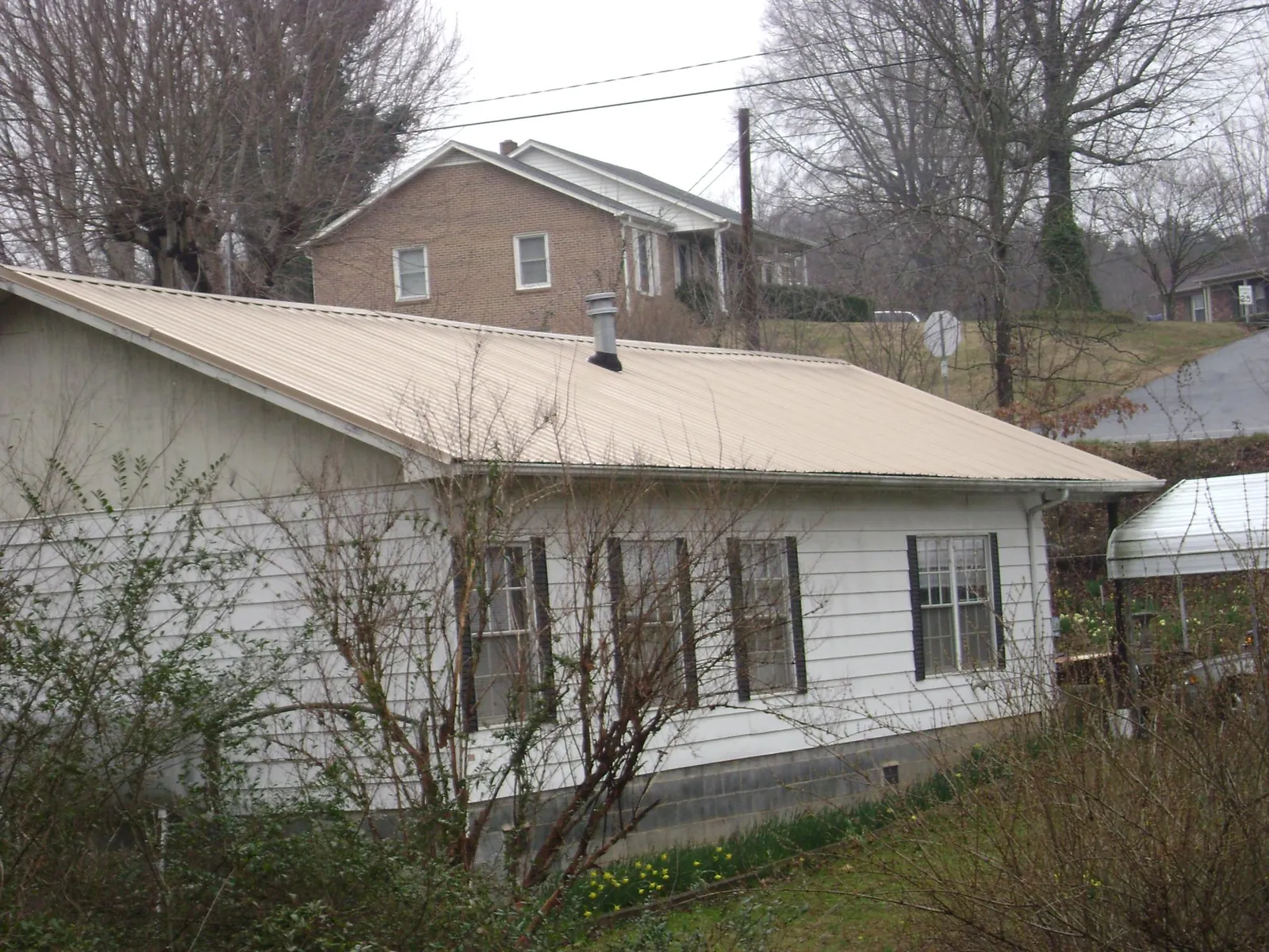 Tan metal roof on a white sided house set into a hillside — Commercial Roofing by Roofing Brothers in Randolph